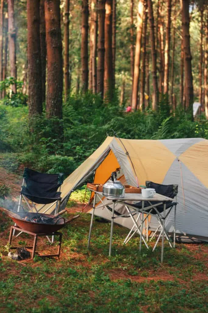 Camping setup with tent and cooking gear in a forest for outdoor pancake making.