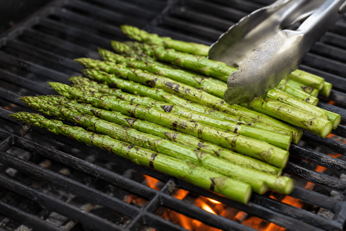 Grilled asparagus spears being turned with tongs