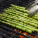 Grilled asparagus spears being turned with tongs