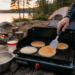 Pancakes cooking on a portable griddle at a campsite beside a lake