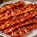 Crisp cooked bacon strips drained on a plate after baking in the oven