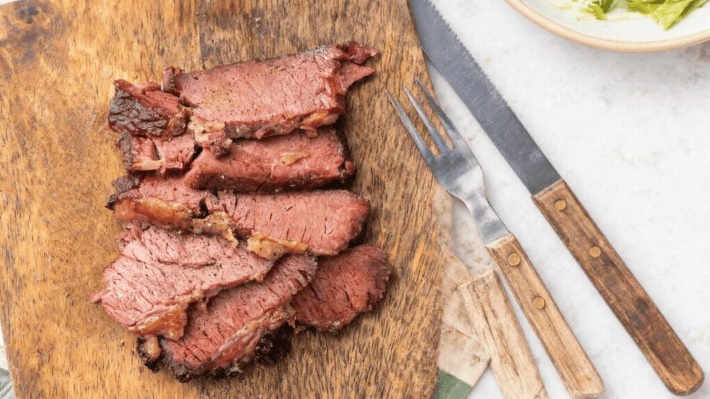 Sliced beef on a wooden board beside a knife