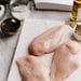 Raw chicken breasts beside salt, pepper, and other kitchen ingredients