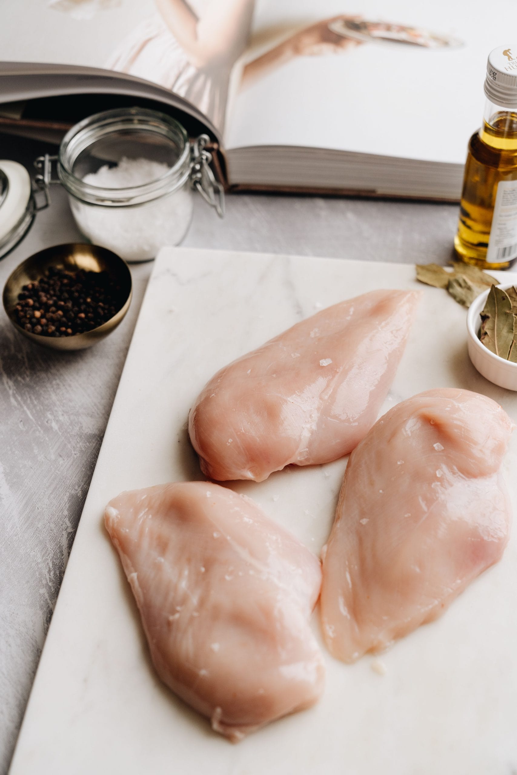 Raw chicken breasts with visibly thicker and thinner ends beside seasonings