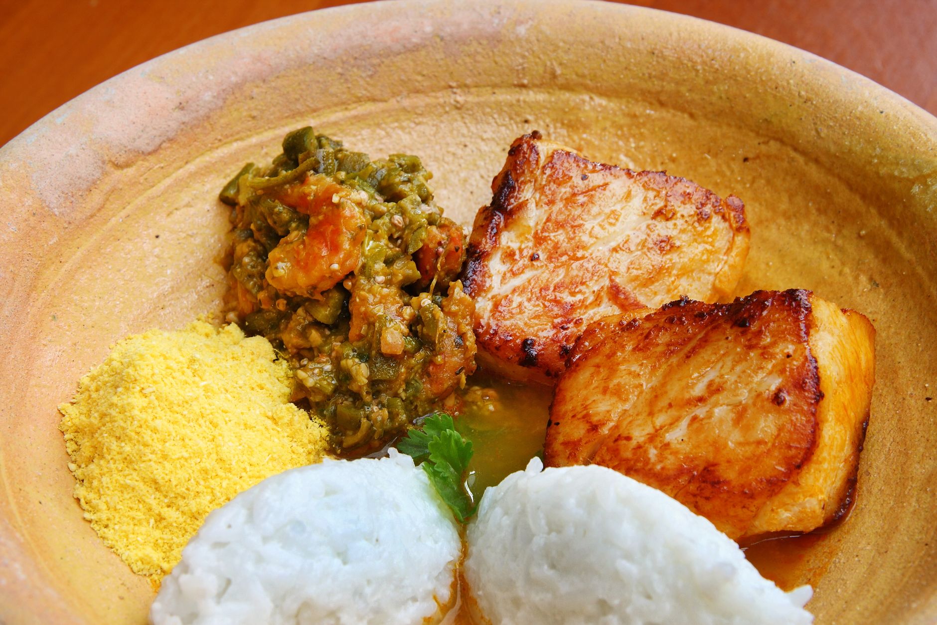 Close-up of grilled fish fillet with rice, couscous and vegetables on a clay plate