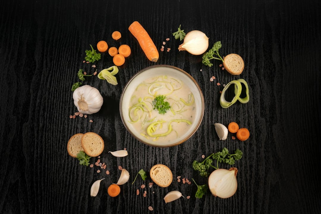Thick creamy vegetable soup surrounded by carrots, onion, garlic, bread, and herbs