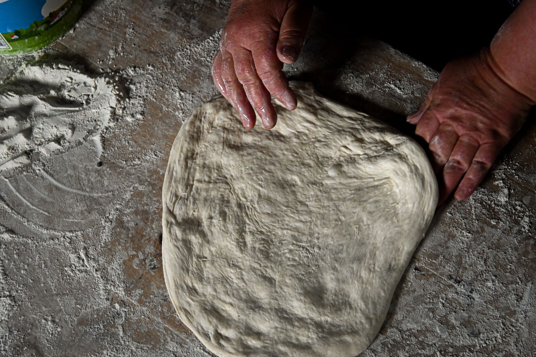 How to prepare homemade pizza: hands stretching dough on a floured work surface