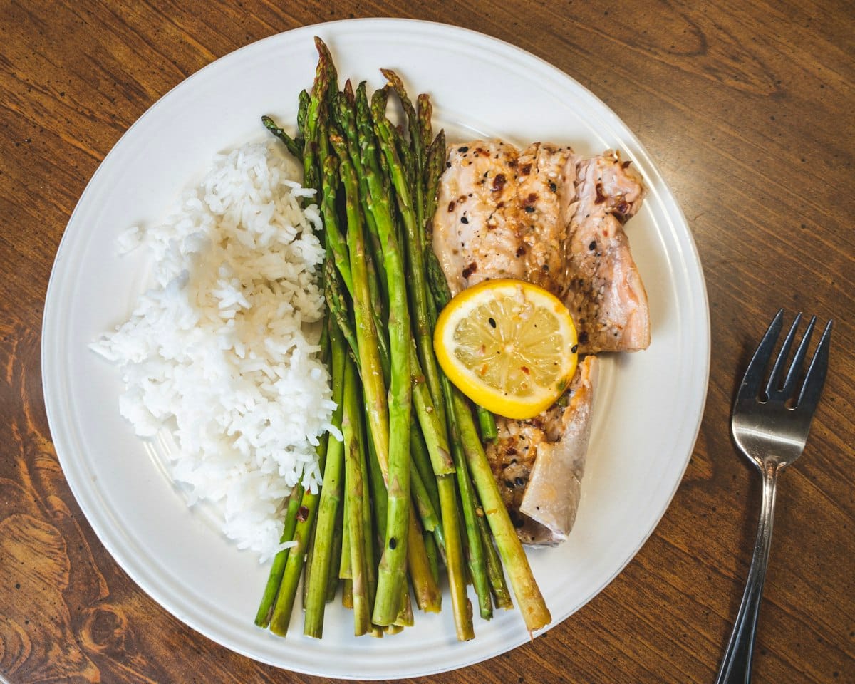 Roasted asparagus with lemon served alongside fish and rice on a dinner plate