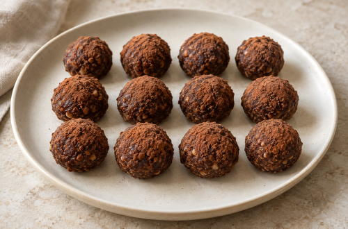 Twelve black olive cocoa date truffles arranged in rows on a cream platter