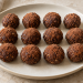 Twelve black olive cocoa date truffles arranged in rows on a cream platter