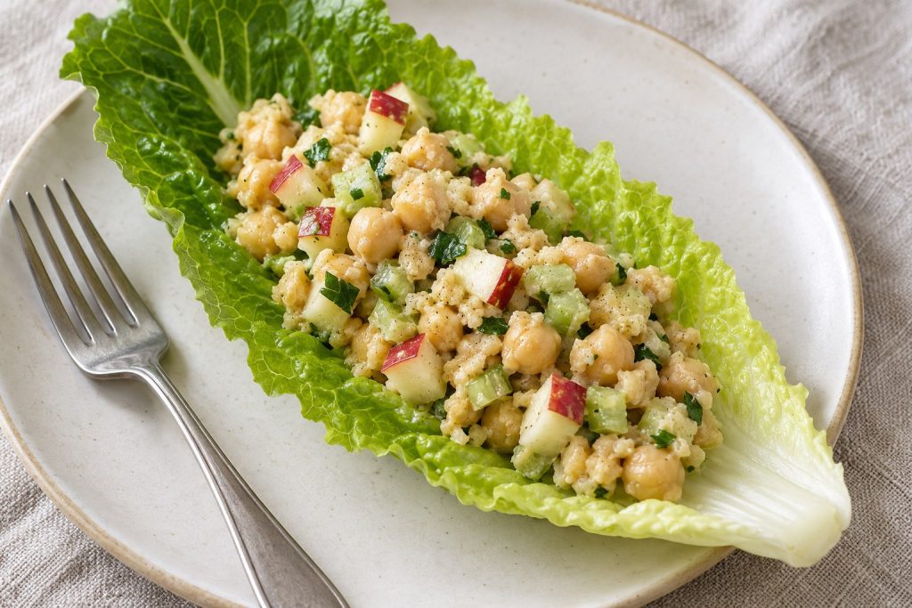 A single romaine leaf holds a modest mound of partly mashed chickpeas, diced apple, celery and parsley, with the leaf edges visible.