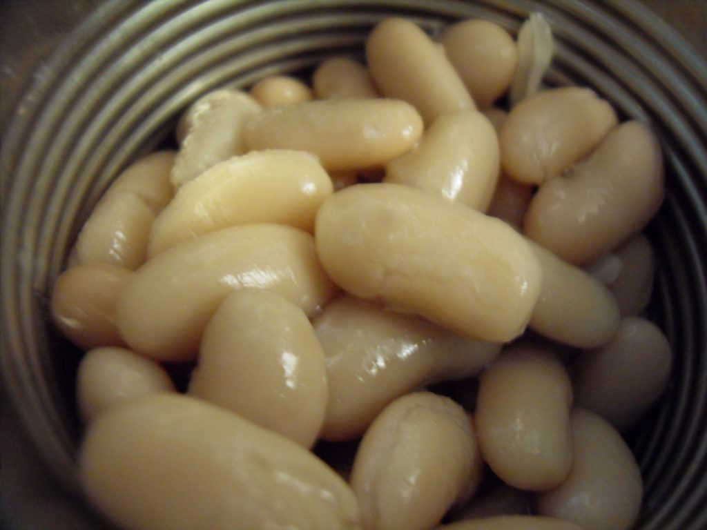 Drained canned white beans with pale skins and mostly intact shapes.