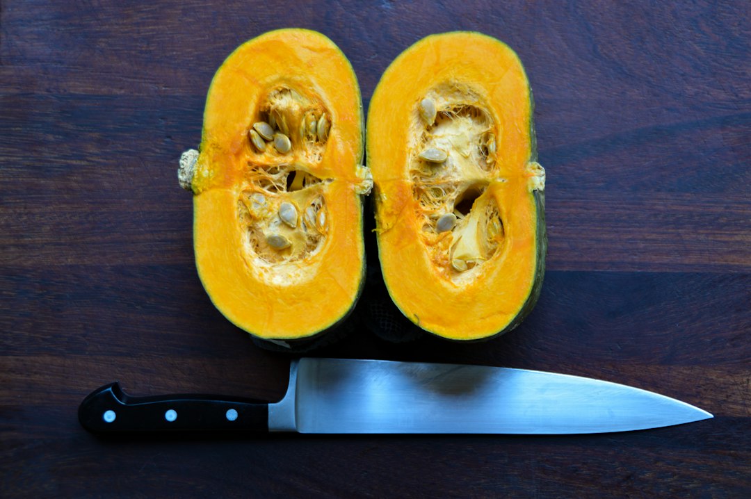 Two acorn squash halves showing green skin and orange flesh on a dark wooden board