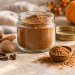 Glass jar of homemade pumpkin spice with a wooden spoon, cinnamon sticks, nutmeg and cloves.