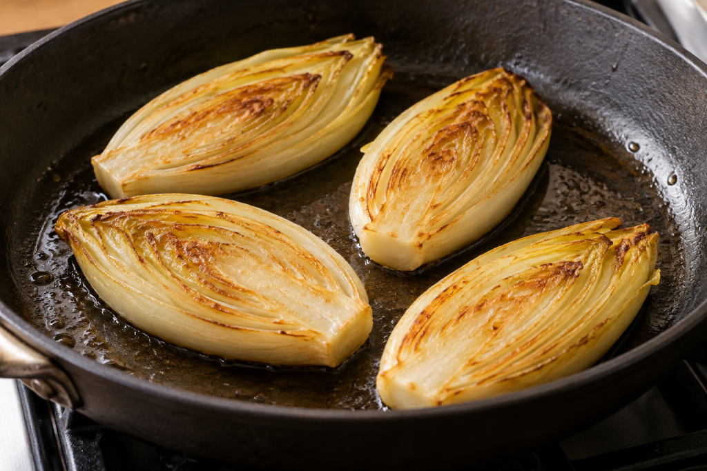 Golden cut sides of pan seared Belgian endive without wine in a cast-iron skillet