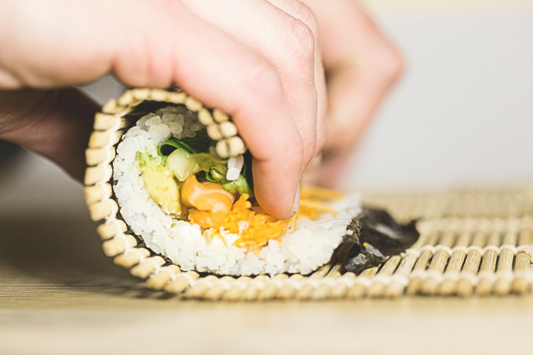 Hands rolling rice, vegetables and seaweed with a bamboo sushi mat