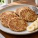 Small golden banana oat pancakes arranged on a plate with a few banana slices.