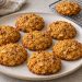 Eight soft orange-gold pumpkin oat cookies with chopped walnuts and lightly browned edges.