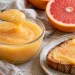 A small glass bowl of pale grapefruit curd beside toast and a halved pink grapefruit